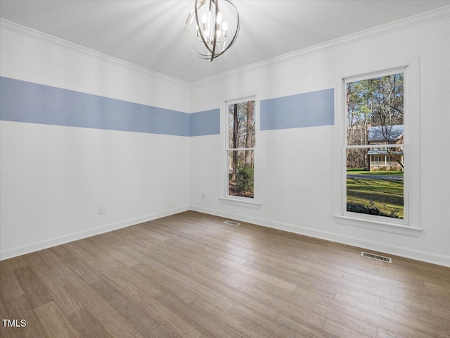 empty room with a notable chandelier, wood finished floors, visible vents, and ornamental molding