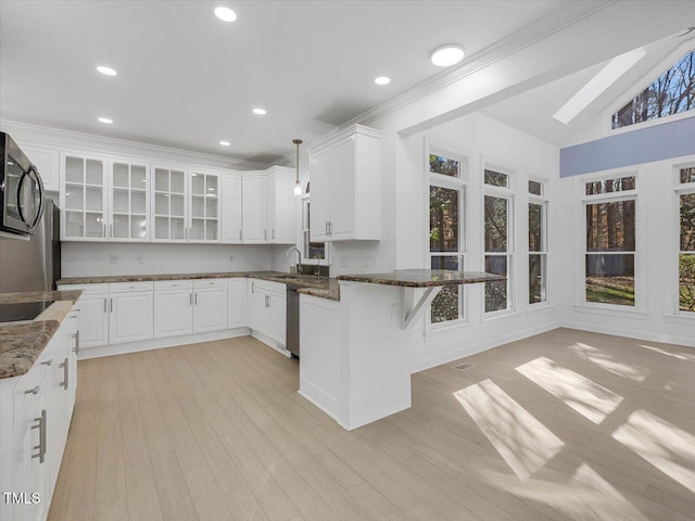 kitchen featuring a breakfast bar, a peninsula, dark stone counters, glass insert cabinets, and black microwave