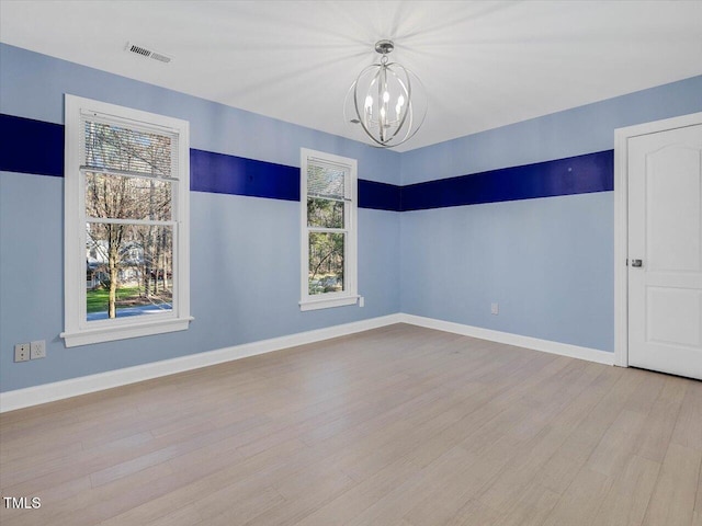 empty room with a notable chandelier, visible vents, baseboards, and wood finished floors