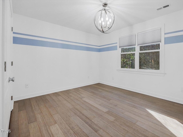 spare room with visible vents, baseboards, a notable chandelier, and wood finished floors