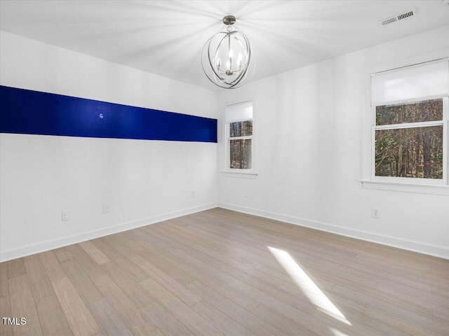 spare room featuring visible vents, baseboards, an inviting chandelier, and wood finished floors