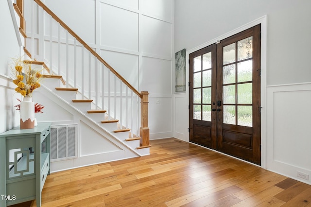 entryway with visible vents, stairs, light wood-type flooring, french doors, and a decorative wall