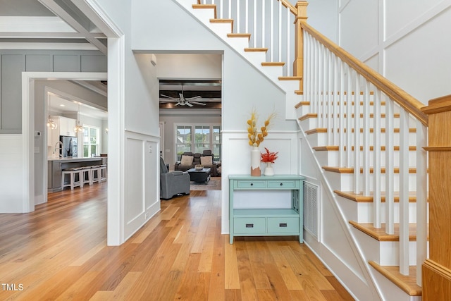 staircase featuring beamed ceiling, a ceiling fan, wood-type flooring, a high ceiling, and a decorative wall