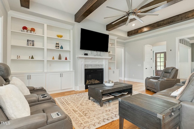 living room featuring light wood-type flooring, beamed ceiling, baseboards, and a high end fireplace