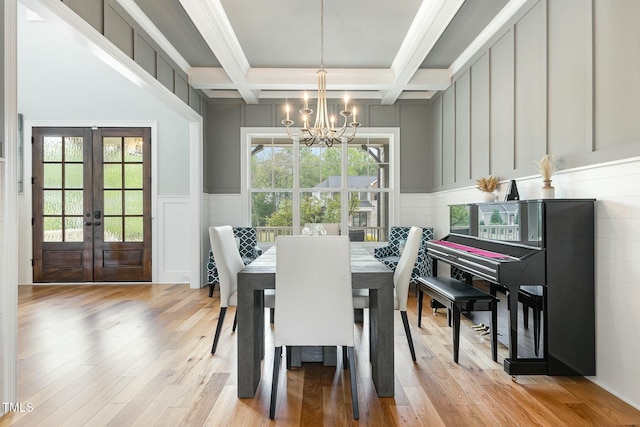 dining room with light wood-type flooring, a notable chandelier, beamed ceiling, and a decorative wall