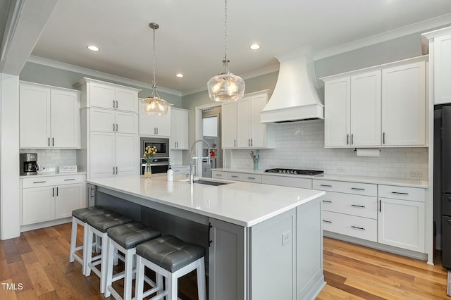 kitchen with premium range hood, a breakfast bar area, light countertops, gas cooktop, and a sink