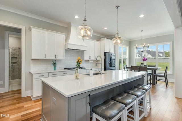 kitchen featuring premium range hood, a breakfast bar, stainless steel refrigerator with ice dispenser, a sink, and gas stovetop