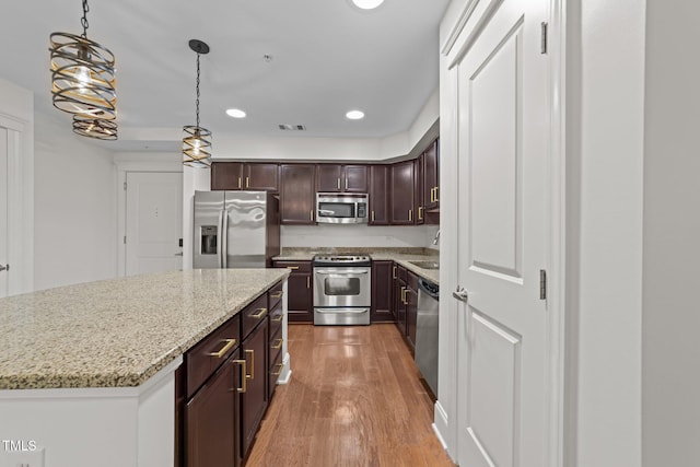 kitchen with light wood finished floors, visible vents, dark brown cabinetry, decorative light fixtures, and stainless steel appliances