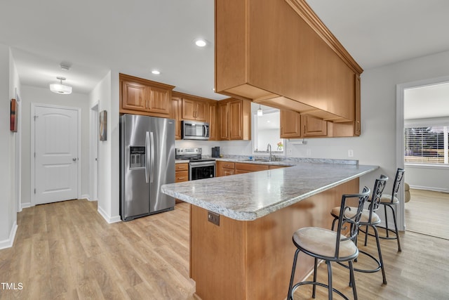 kitchen with a sink, appliances with stainless steel finishes, a peninsula, brown cabinetry, and light countertops