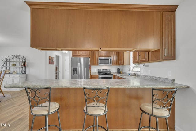 kitchen featuring a sink, stainless steel appliances, a peninsula, brown cabinetry, and light countertops