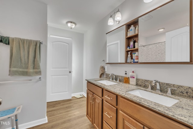 full bathroom featuring double vanity, wood finished floors, baseboards, and a sink