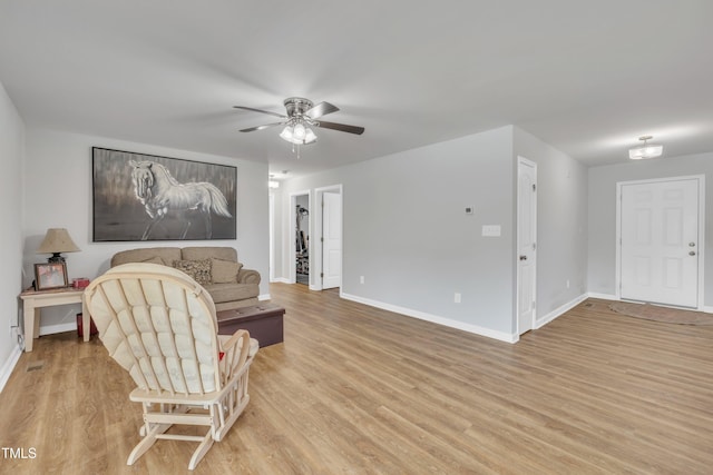 living area with baseboards, a ceiling fan, and light wood finished floors