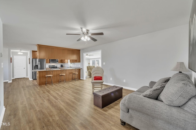 living room with light wood-type flooring, baseboards, and ceiling fan