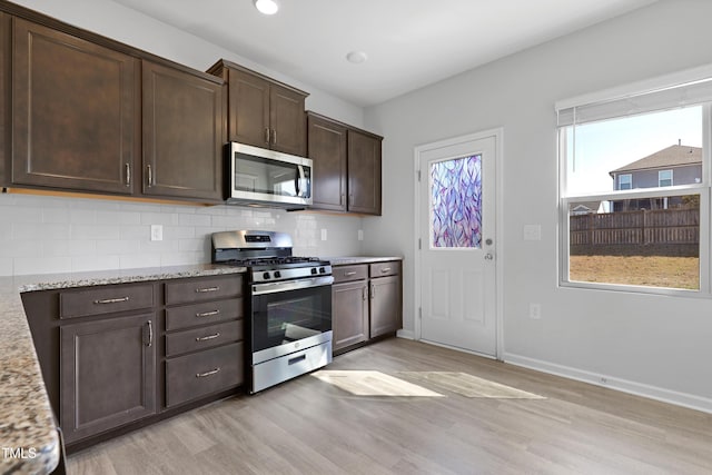 kitchen with dark brown cabinetry, stainless steel appliances, light wood-type flooring, and tasteful backsplash