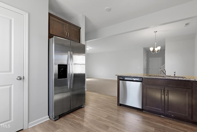 kitchen with a sink, light stone counters, appliances with stainless steel finishes, light wood finished floors, and dark brown cabinets