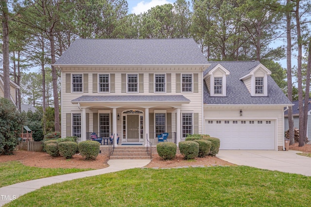 colonial house featuring a front lawn, concrete driveway, roof with shingles, covered porch, and a garage