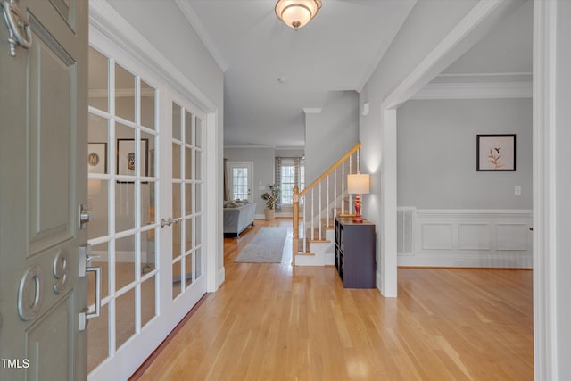 foyer featuring stairway, wood finished floors, a wainscoted wall, ornamental molding, and french doors