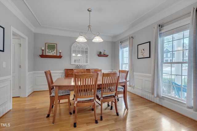 dining space with light wood finished floors, wainscoting, crown molding, and an inviting chandelier