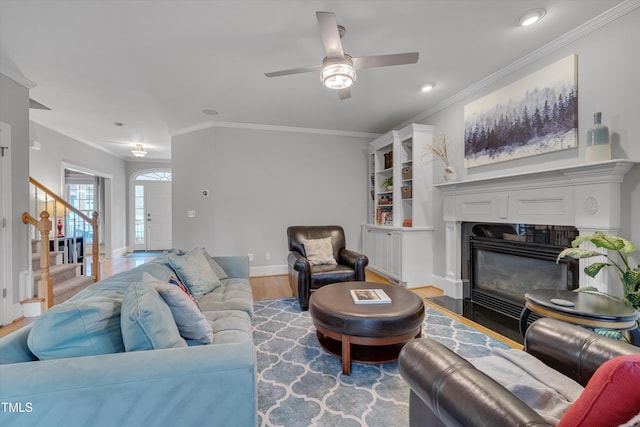 living area featuring stairway, wood finished floors, baseboards, a fireplace with flush hearth, and ornamental molding