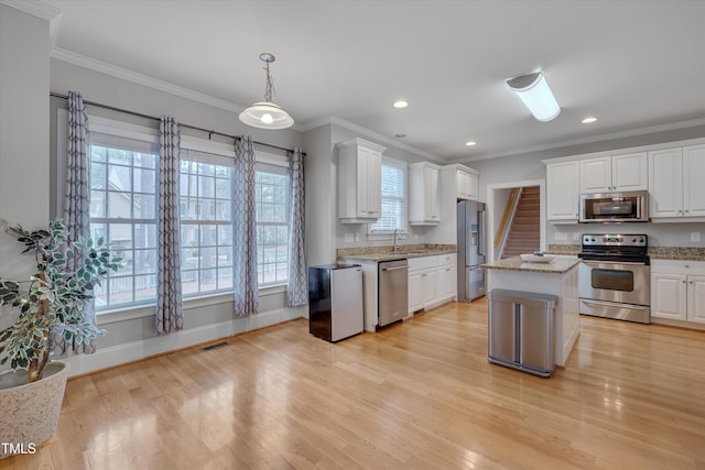 kitchen with light stone counters, ornamental molding, white cabinets, appliances with stainless steel finishes, and light wood-type flooring