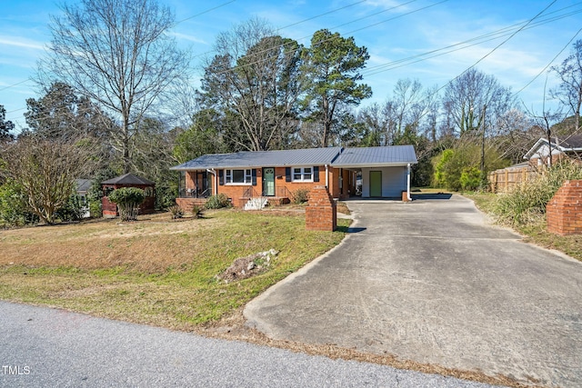 ranch-style home featuring brick siding, a front lawn, metal roof, a carport, and driveway