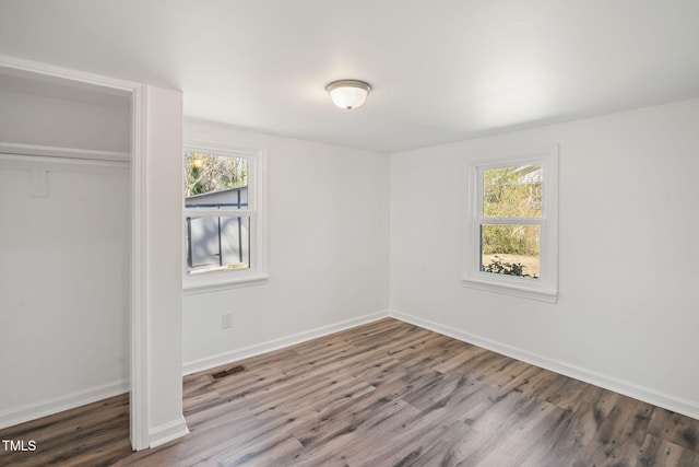 unfurnished bedroom featuring visible vents, multiple windows, baseboards, and wood finished floors