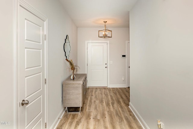 hall featuring a notable chandelier, light wood-type flooring, and baseboards