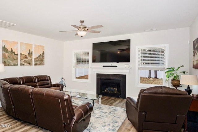 living room with ceiling fan, visible vents, a glass covered fireplace, and light wood finished floors