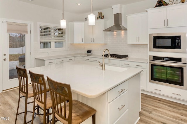 kitchen featuring light wood-style flooring, stainless steel appliances, wall chimney exhaust hood, and light countertops