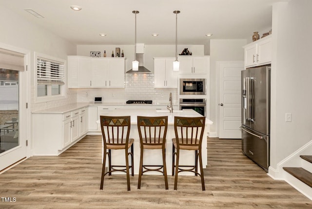 kitchen with light wood-type flooring, stainless steel appliances, light countertops, and wall chimney range hood