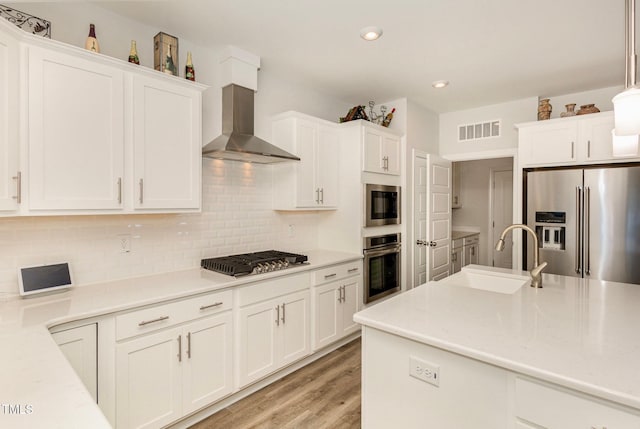 kitchen with visible vents, white cabinets, stainless steel appliances, wall chimney exhaust hood, and a sink