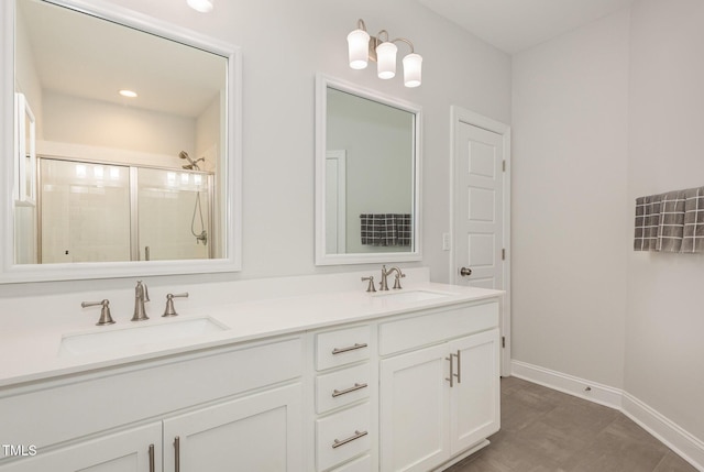 bathroom with double vanity, a stall shower, baseboards, and a sink