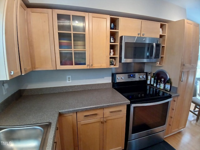 kitchen featuring dark countertops, open shelves, light brown cabinetry, appliances with stainless steel finishes, and a sink