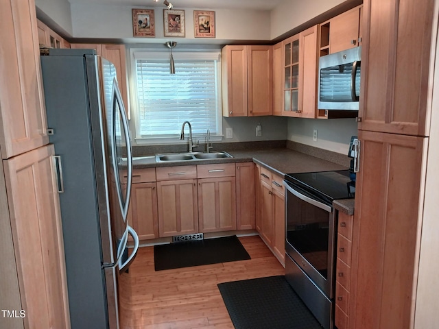 kitchen with light wood finished floors, a sink, light brown cabinetry, stainless steel appliances, and dark countertops