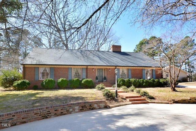 ranch-style house with brick siding, a chimney, and a front yard