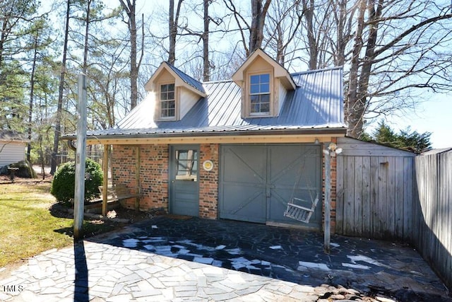 view of front of home with brick siding, an attached garage, metal roof, and fence