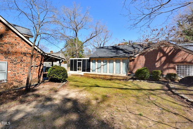 rear view of house featuring a yard, brick siding, and a sunroom