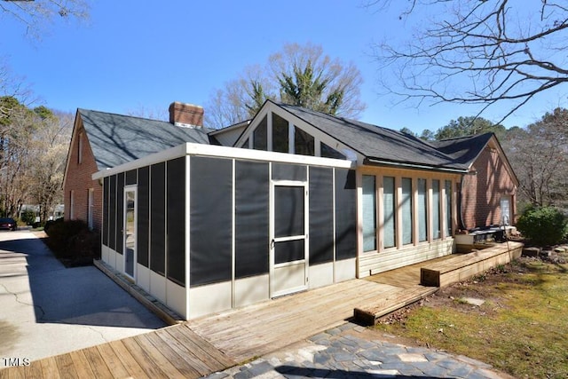 view of property exterior with a wooden deck, a chimney, brick siding, and a sunroom