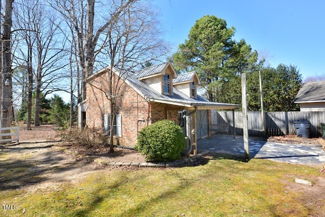 view of home's exterior with a lawn, fence, brick siding, and metal roof