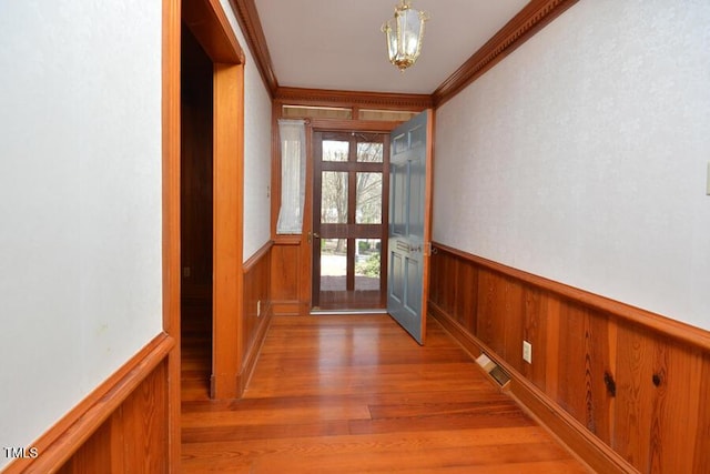 entryway featuring visible vents, ornamental molding, wainscoting, and light wood-style flooring