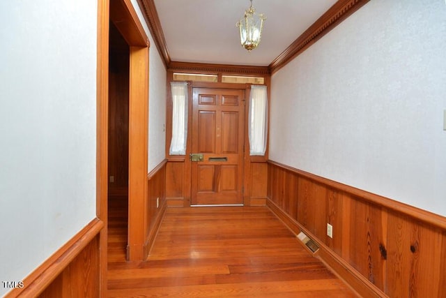 hallway featuring crown molding, light wood-style floors, visible vents, and wainscoting