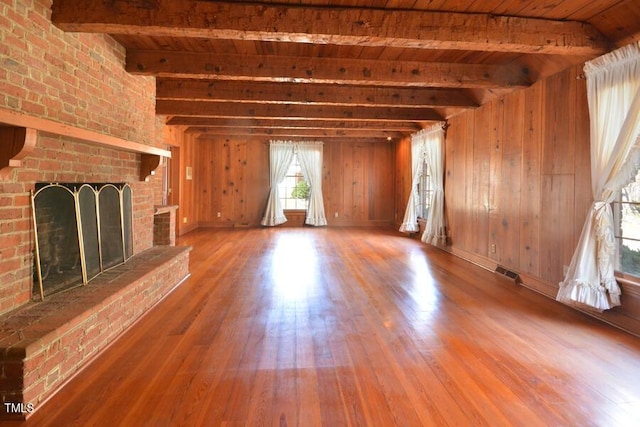 unfurnished living room featuring beamed ceiling, wood walls, a fireplace, and wood finished floors