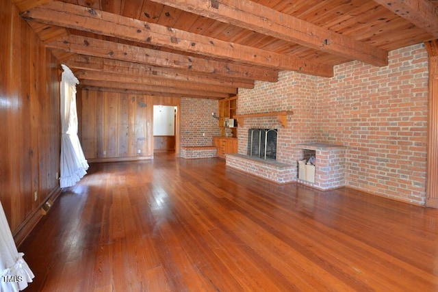 unfurnished living room with hardwood / wood-style floors, wooden walls, brick wall, beam ceiling, and a fireplace