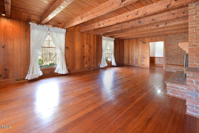 unfurnished living room featuring wooden walls, visible vents, hardwood / wood-style flooring, wooden ceiling, and beamed ceiling