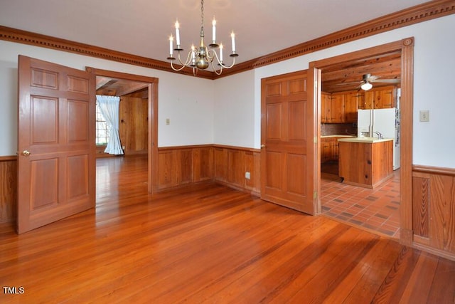 unfurnished dining area with a chandelier, light wood-style flooring, wainscoting, and ornamental molding