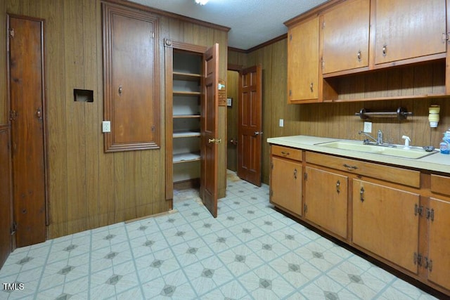 kitchen featuring light floors, light countertops, ornamental molding, brown cabinetry, and a sink