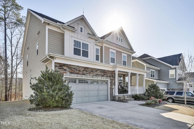 view of front of home with driveway, covered porch, a garage, stone siding, and board and batten siding