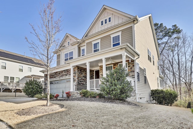 view of front of home with stone siding, a porch, fence, board and batten siding, and a garage