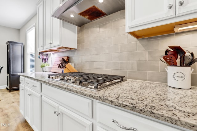 kitchen featuring backsplash, white cabinetry, wall chimney range hood, and stainless steel gas stovetop