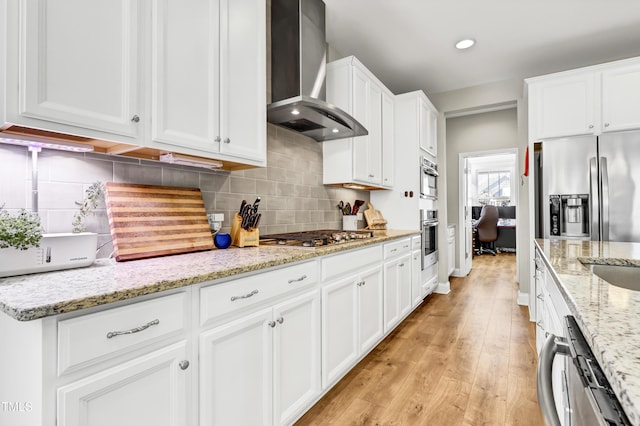 kitchen with tasteful backsplash, white cabinetry, stainless steel appliances, and wall chimney range hood